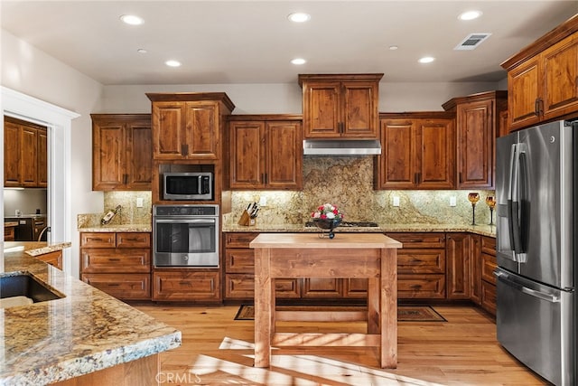 kitchen with light stone counters, appliances with stainless steel finishes, light wood-type flooring, and backsplash