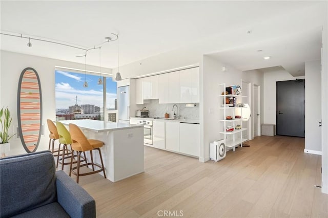 kitchen featuring pendant lighting, white cabinets, oven, decorative backsplash, and light hardwood / wood-style floors