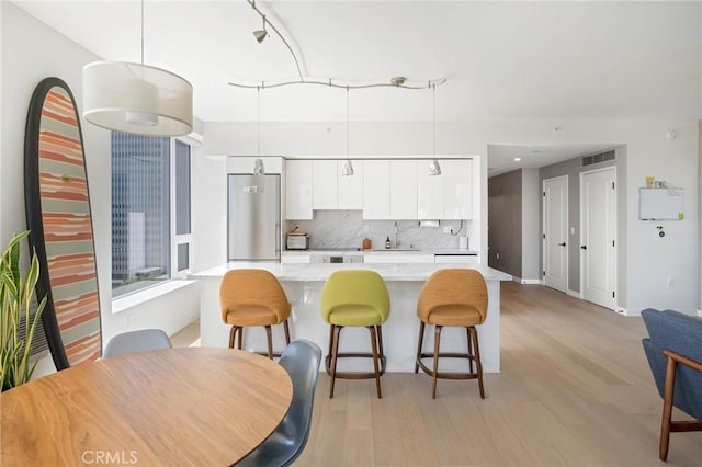 kitchen featuring a kitchen breakfast bar, sink, decorative light fixtures, white cabinetry, and stainless steel refrigerator