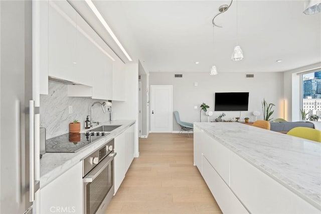 kitchen with stainless steel oven, black electric stovetop, refrigerator, sink, and white cabinetry