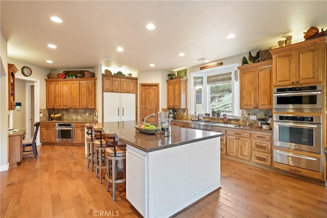 kitchen featuring built in refrigerator, light hardwood / wood-style flooring, dark stone counters, and a center island