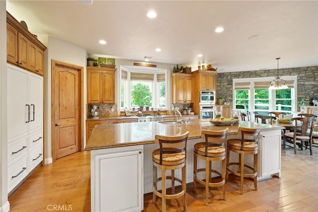 kitchen featuring pendant lighting, light hardwood / wood-style flooring, a center island with sink, and sink