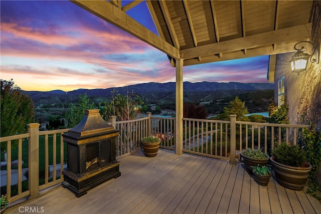 deck at dusk featuring an outdoor fireplace and a mountain view