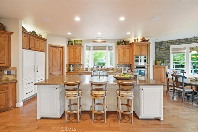 kitchen with light wood-type flooring, double oven, an island with sink, and a breakfast bar area