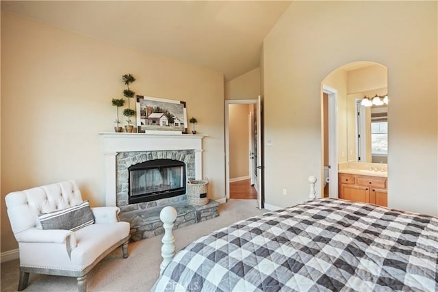 carpeted bedroom with vaulted ceiling, ensuite bath, and a fireplace