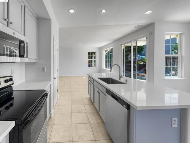 kitchen with decorative backsplash, appliances with stainless steel finishes, a kitchen island with sink, light tile patterned flooring, and sink