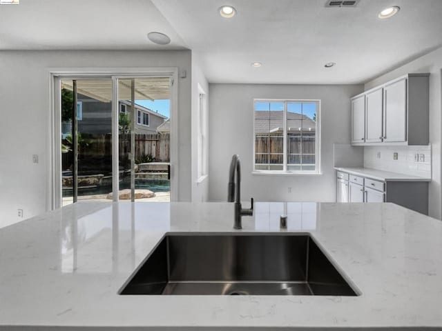 kitchen with gray cabinetry, light stone countertops, sink, and decorative backsplash