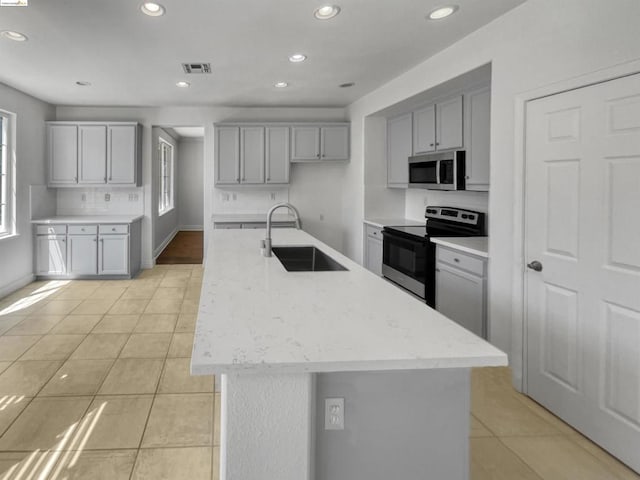 kitchen with sink, stainless steel appliances, gray cabinets, light tile patterned floors, and a center island with sink