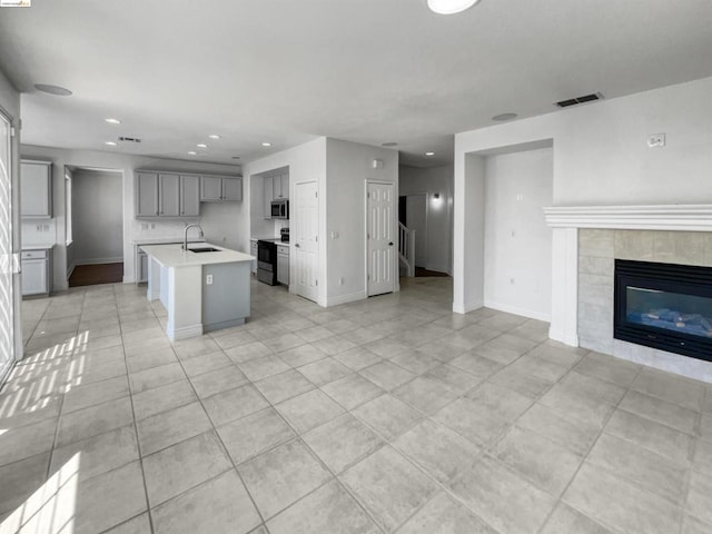 kitchen featuring an island with sink, black / electric stove, light tile patterned flooring, a tile fireplace, and sink