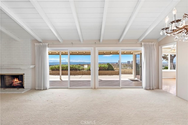 unfurnished living room with carpet, beam ceiling, a fireplace, and ceiling fan with notable chandelier