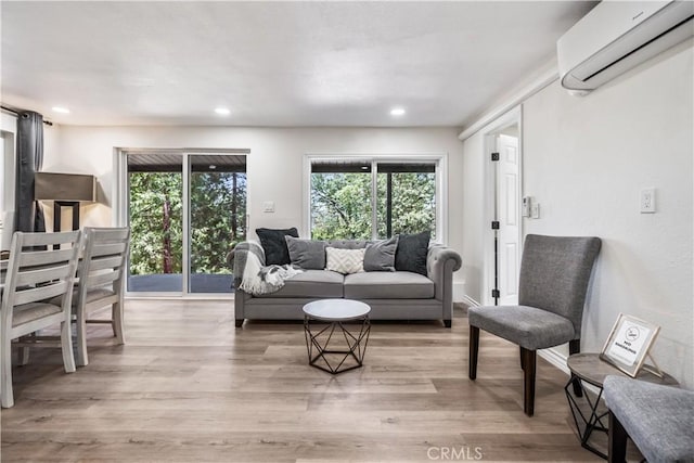 living room with an AC wall unit, a wealth of natural light, and light hardwood / wood-style flooring