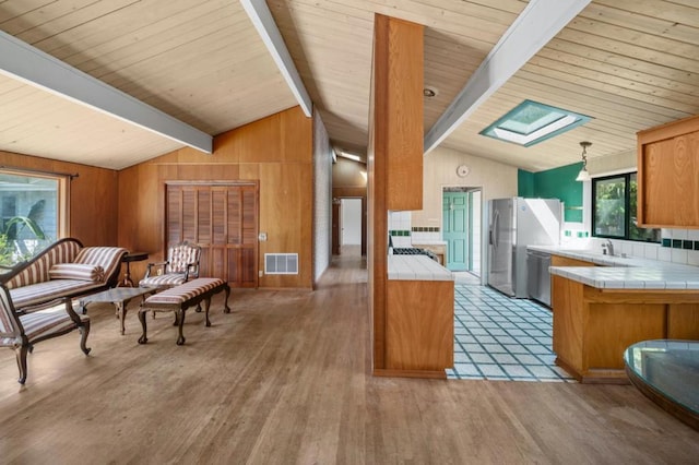 kitchen featuring stainless steel appliances, tile countertops, light hardwood / wood-style floors, and lofted ceiling with skylight