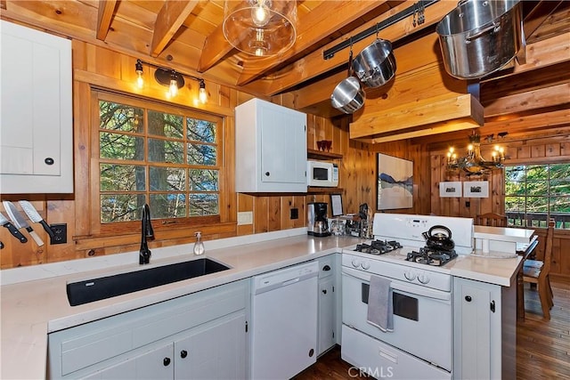 kitchen with pendant lighting, white appliances, white cabinets, wooden walls, and kitchen peninsula