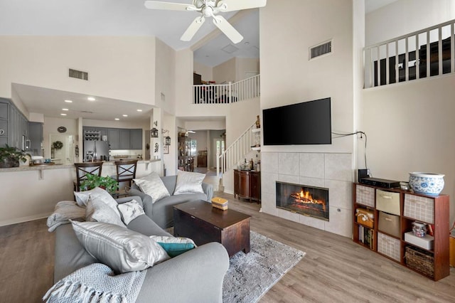 living room featuring a fireplace, ceiling fan, light hardwood / wood-style flooring, and high vaulted ceiling