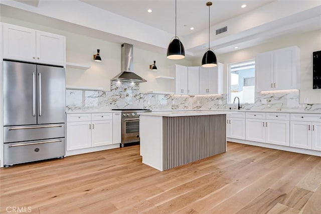 kitchen with wall chimney exhaust hood, high quality appliances, and white cabinetry