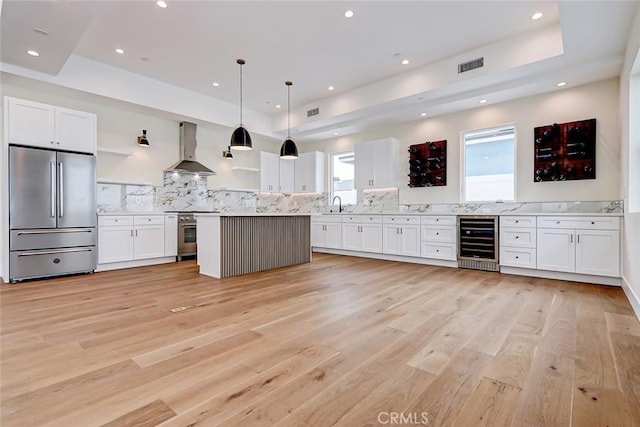 kitchen with wall chimney exhaust hood, appliances with stainless steel finishes, decorative light fixtures, white cabinetry, and beverage cooler