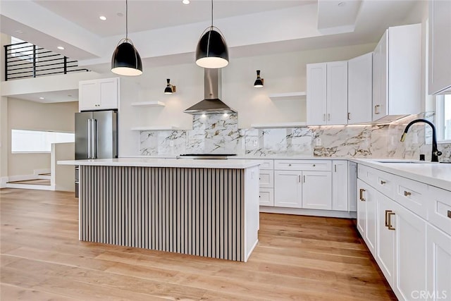 kitchen featuring white cabinets, pendant lighting, wall chimney range hood, and light wood-type flooring