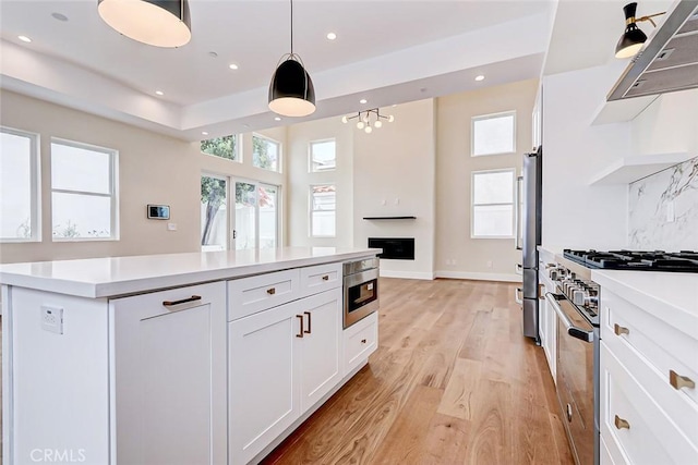 kitchen with stainless steel appliances, pendant lighting, light hardwood / wood-style flooring, white cabinets, and range hood