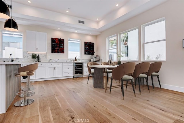 kitchen featuring white cabinets, light hardwood / wood-style flooring, beverage cooler, and hanging light fixtures