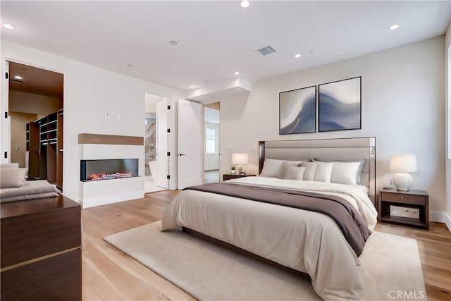 bedroom with ensuite bathroom, light hardwood / wood-style floors, and a spacious closet