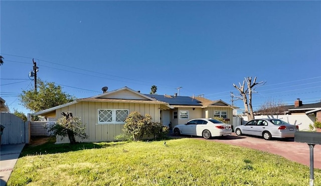 single story home featuring board and batten siding, a front yard, fence, and roof mounted solar panels