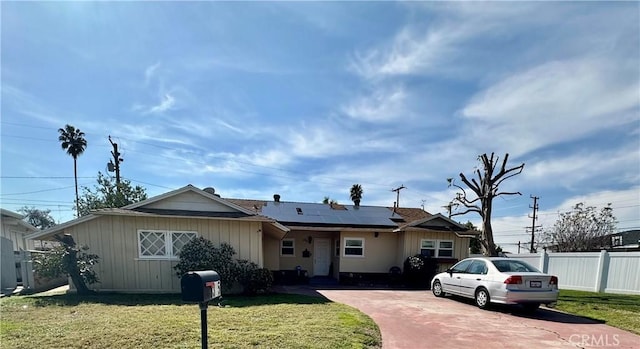 ranch-style house with driveway, solar panels, fence, and a front yard