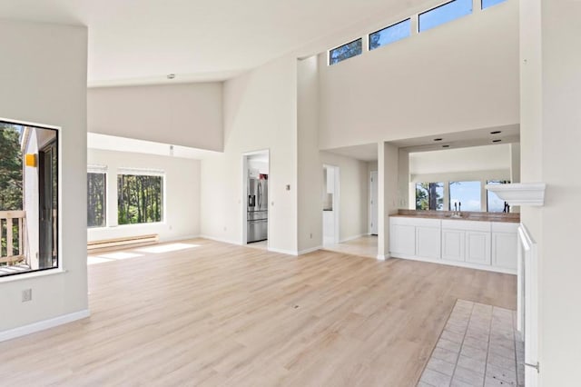 unfurnished living room featuring high vaulted ceiling, sink, light hardwood / wood-style flooring, and a baseboard radiator