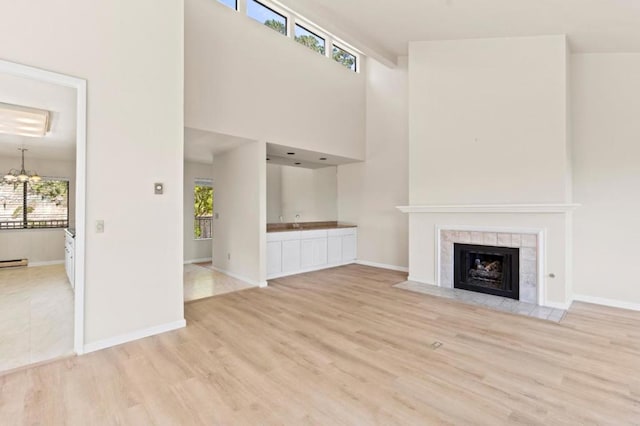 unfurnished living room with a high ceiling, sink, a notable chandelier, light hardwood / wood-style flooring, and a tiled fireplace