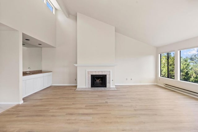 unfurnished living room with baseboard heating, lofted ceiling, sink, light wood-type flooring, and a tile fireplace