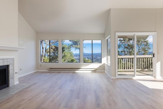 unfurnished living room with a mountain view, light wood-type flooring, baseboard heating, lofted ceiling, and a fireplace