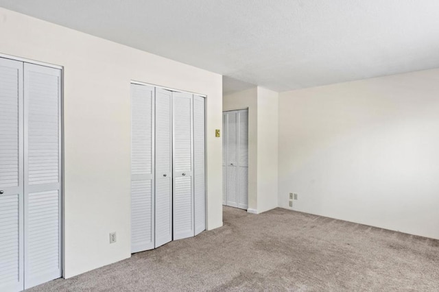 unfurnished bedroom with two closets and light carpet