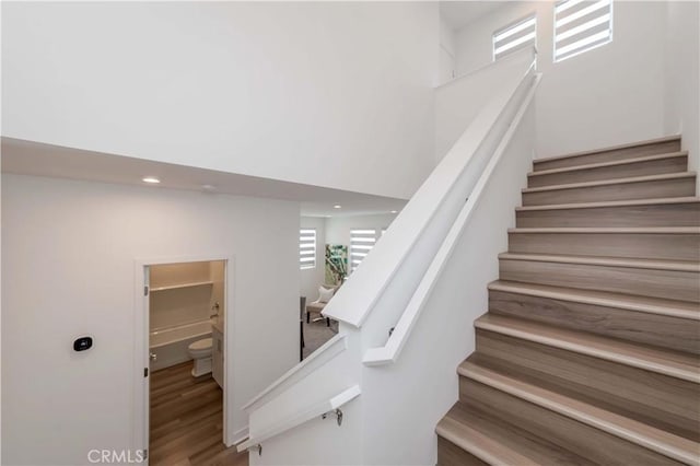 stairway with wood-type flooring and a towering ceiling