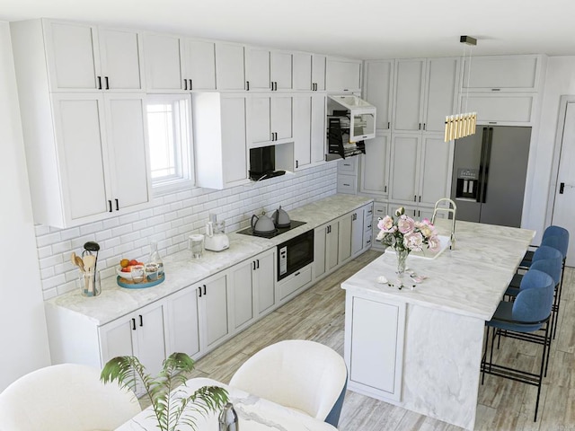 kitchen featuring a kitchen island with sink, a breakfast bar, black appliances, tasteful backsplash, and light hardwood / wood-style floors