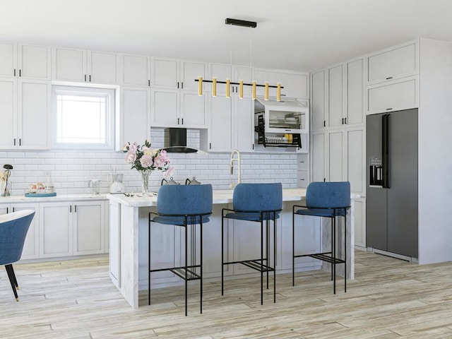 kitchen featuring backsplash, a kitchen breakfast bar, refrigerator with ice dispenser, and white cabinets