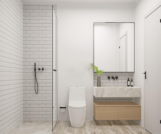 bathroom featuring wood-type flooring, tiled shower, vanity with extensive cabinet space, and toilet