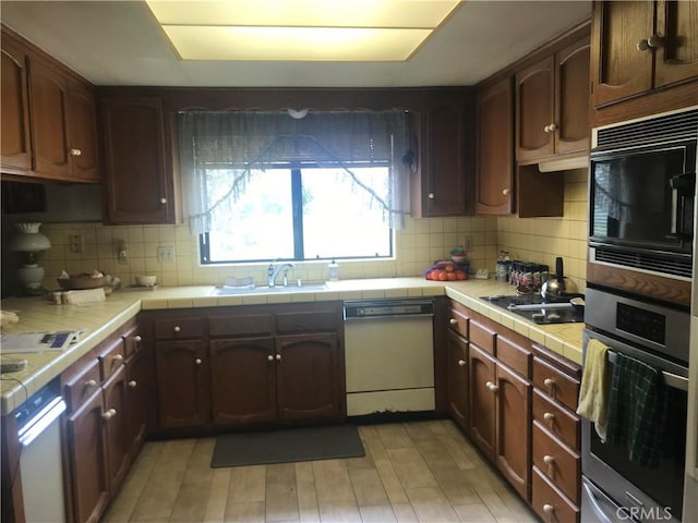 kitchen featuring sink, tile countertops, light hardwood / wood-style floors, decorative backsplash, and black appliances