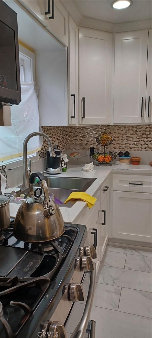 kitchen with decorative backsplash, stainless steel range oven, white cabinetry, and sink