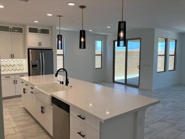 kitchen with white cabinetry, sink, hanging light fixtures, an island with sink, and appliances with stainless steel finishes