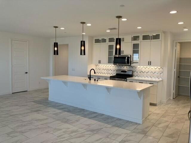 kitchen with white cabinetry, hanging light fixtures, tasteful backsplash, a kitchen island with sink, and appliances with stainless steel finishes