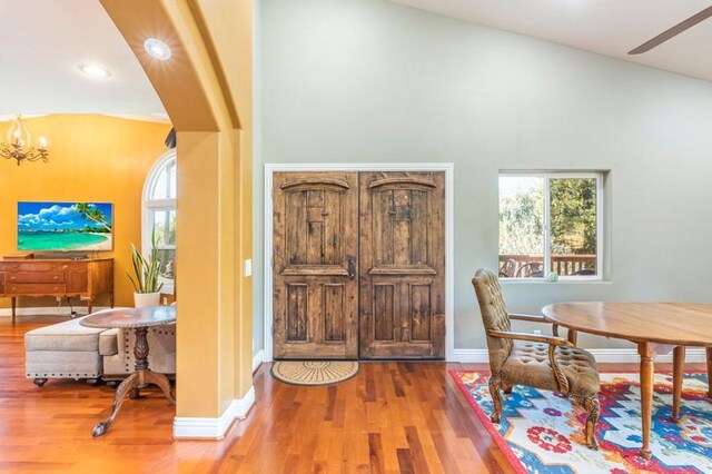 foyer entrance with vaulted ceiling, ceiling fan with notable chandelier, and hardwood / wood-style floors