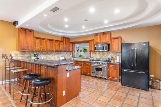 kitchen featuring a kitchen bar, a tray ceiling, backsplash, and appliances with stainless steel finishes