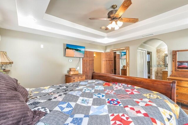 bedroom featuring a tray ceiling, ceiling fan, and ensuite bathroom