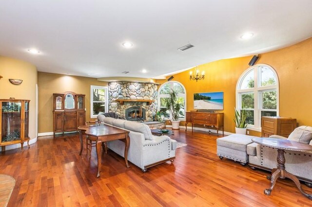 living room with a stone fireplace, a healthy amount of sunlight, hardwood / wood-style floors, and an inviting chandelier