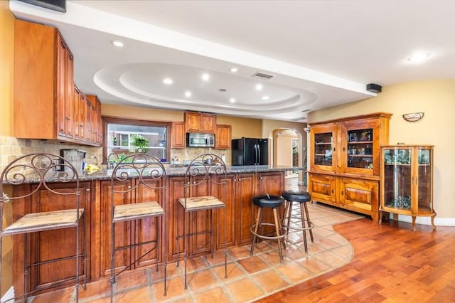 kitchen featuring black fridge, a raised ceiling, a kitchen bar, decorative backsplash, and kitchen peninsula