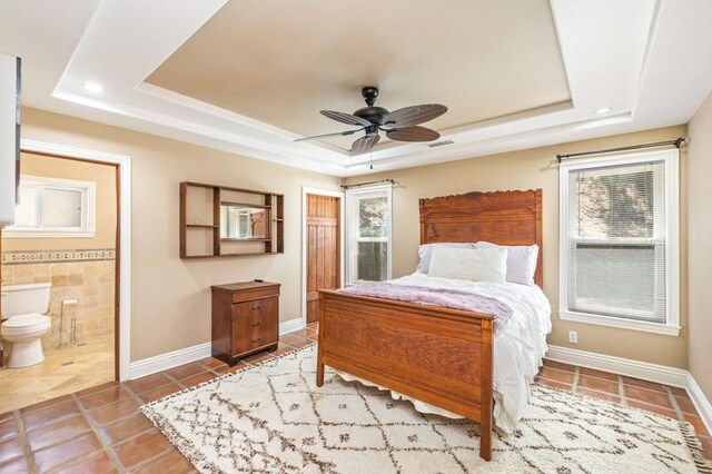 bedroom featuring light tile patterned flooring, a raised ceiling, ceiling fan, and ensuite bathroom