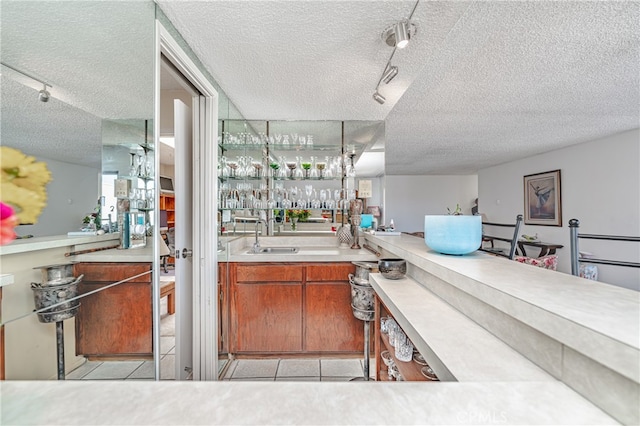 bar featuring sink, light tile flooring, rail lighting, and a textured ceiling