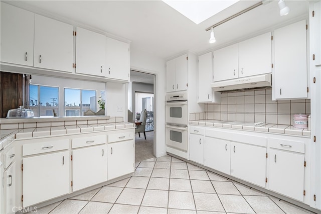 kitchen with rail lighting, double oven, tasteful backsplash, white cabinets, and tile countertops