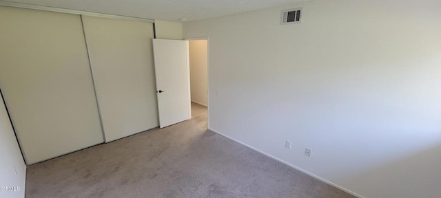 unfurnished bedroom with light colored carpet and a closet