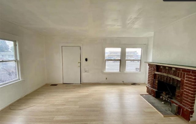 unfurnished living room with light wood-type flooring, a brick fireplace, and plenty of natural light