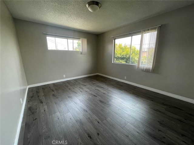 empty room featuring a textured ceiling, dark hardwood / wood-style flooring, and a healthy amount of sunlight